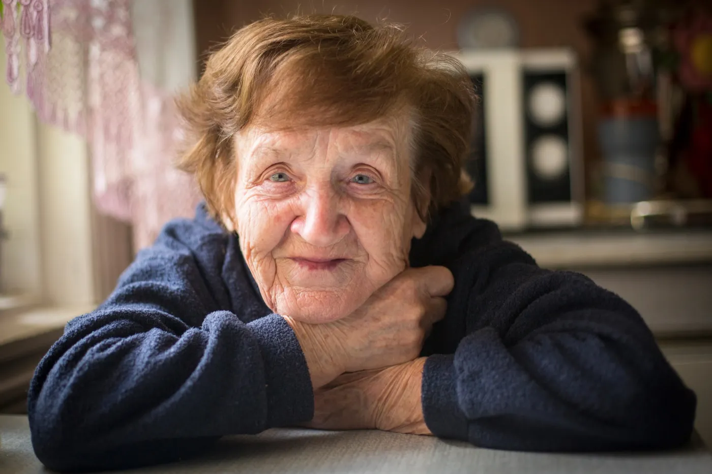 Lächelnde Seniorin an einem Tisch zuhause
